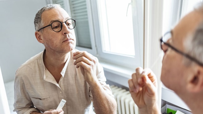 Homem de meia-idade a fazer um autoteste à covid, em frente a um espelho