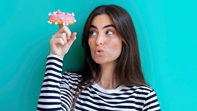 Jovem mulher com donut no dedo sobre fundo azul turquesa