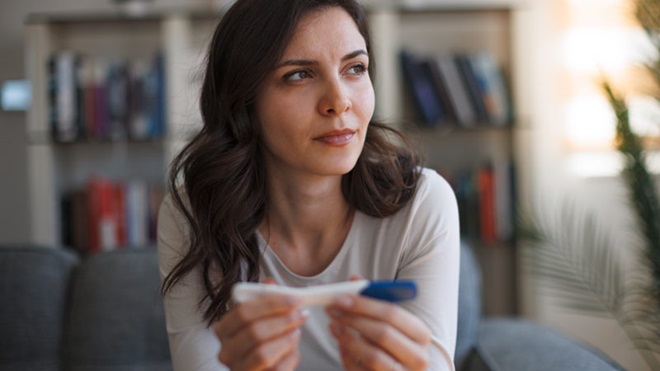 Mulher jovem com ar triste e pensativo com um teste de gravidez nas mãos - alusão ao tema da infertilidade