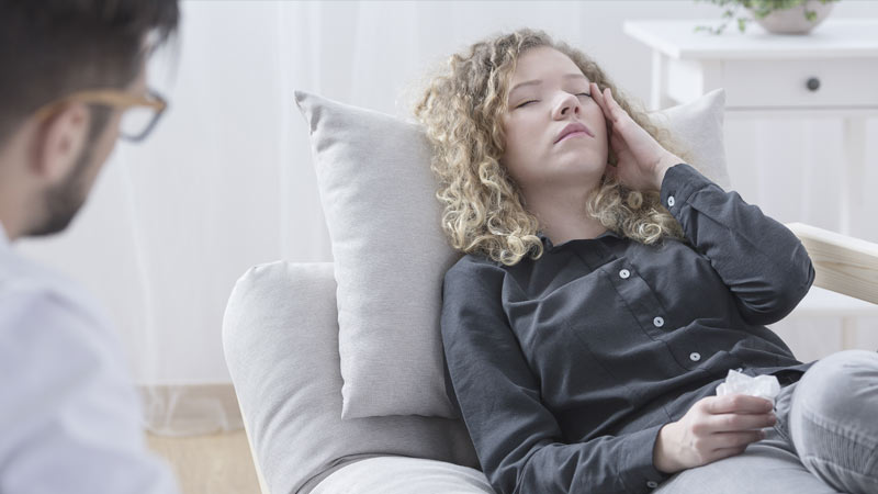 Mulher deitada num sofá com ar adoentado