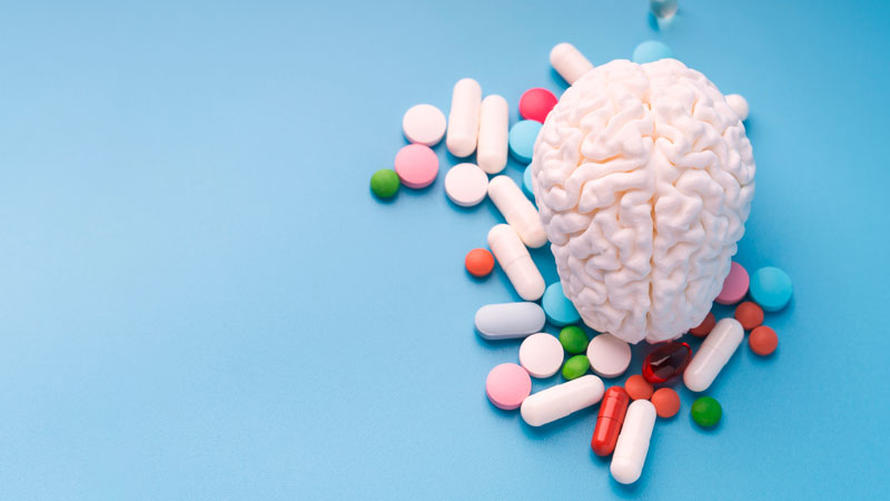 Maquete de um cérebro em plástico em cima de um tampo azul, sobre medicamentos de várias cores