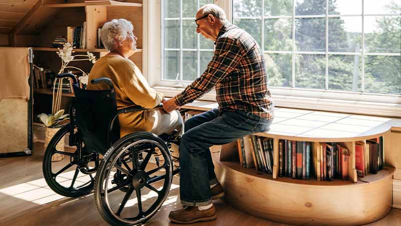 Homem a apoiar mulher idosa em cadeira de rodas em casa