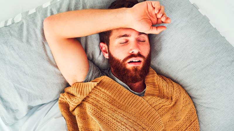Homem deitado na cama com a boca aberta, mostrando mau estar - alusão a ressonar