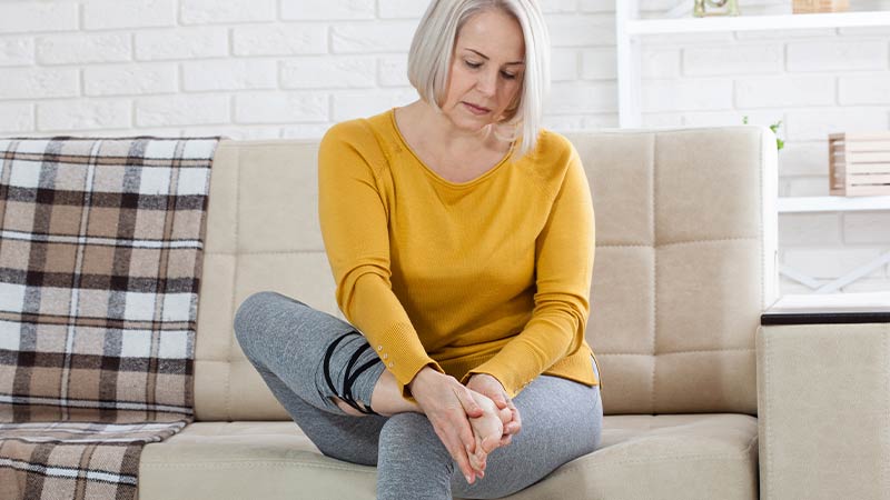 Mulher com roupa desportiva examina o pé em casa