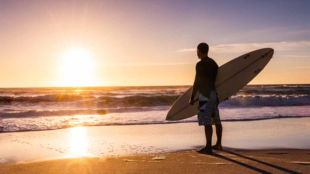 surfista na praia ao pôr do sol com a prancha na mão