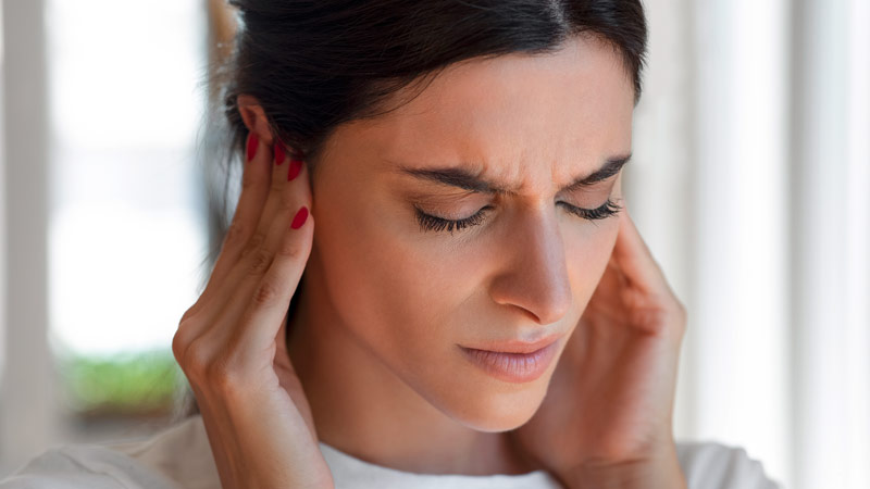 Grande plano de mulher a segurar nos dois ouvidos - alusão a otite externa