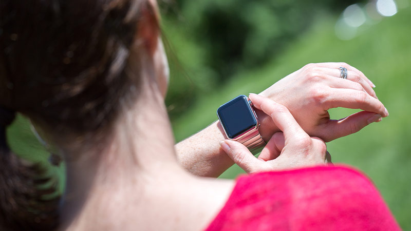 grande plano de mulher de costas a olhar para ecrã de smartwatch