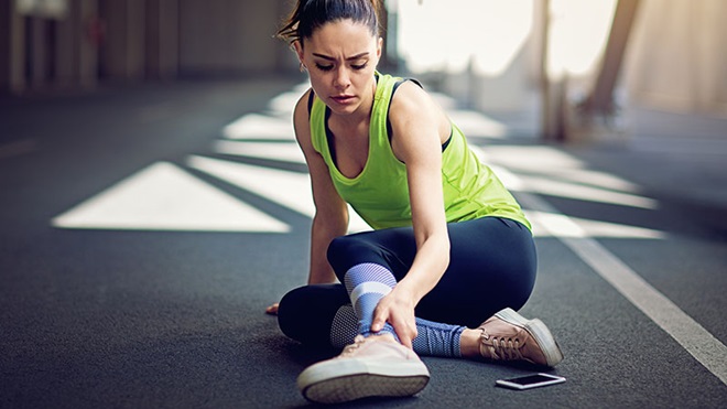 mulher atleta no chão a queixar-se de lesão no tornozelo