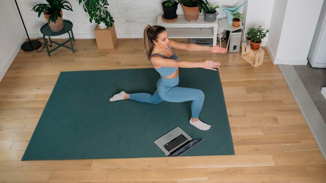 Mulher vestida com roupa de fitness faz exercícios em casa com um computador - alusão a apps de exercício físico