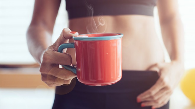 Grande plano de mulher vestida com roupa de fitness a segurar uma caneca de café fumegante