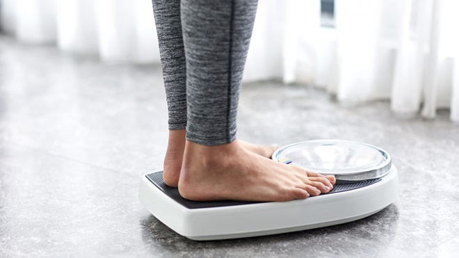 Plano de pormenor com pernas e pés de mulher com calças fitness, a pesar-se numa balança