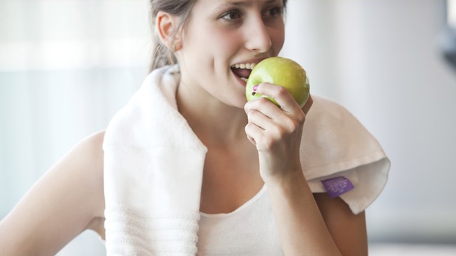 Mulher equipada para uma sessão de desporto a comer uma maçã