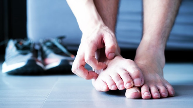 Grande plano de pés de homem com uma mão a coçá-los. fundo azul; ténis desportivos ao fundo