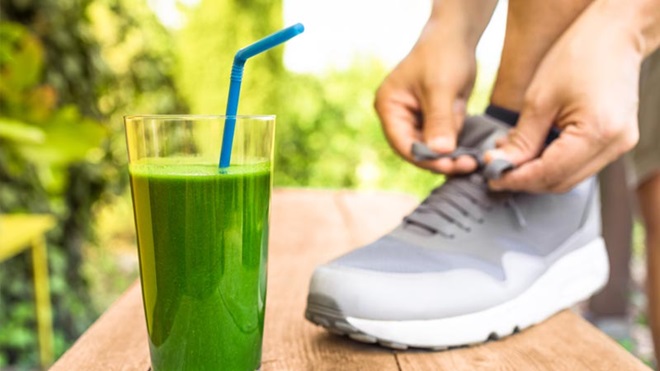 Grande plano de um smoothie de vegetais com um pormenor de um atleta a atar os ténis em fundo