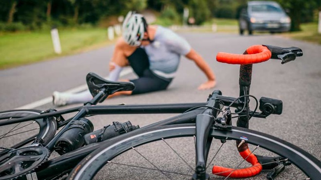 Ciclista ao fundo caído na estrada; bicicleta em primeiro plano