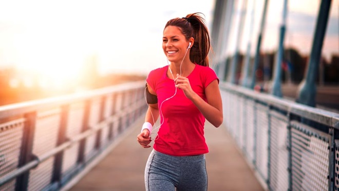 Mulher com ar satisfeito e com roupa de jogging, a correr numa ponte pedonal, com o sol ao fundo