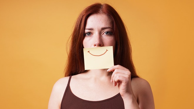 mulher cobre a boca com um post-it amarelo com um sorriso desenhado