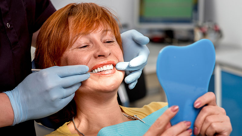 Mulher no dentista a ver a prótese ao espelho