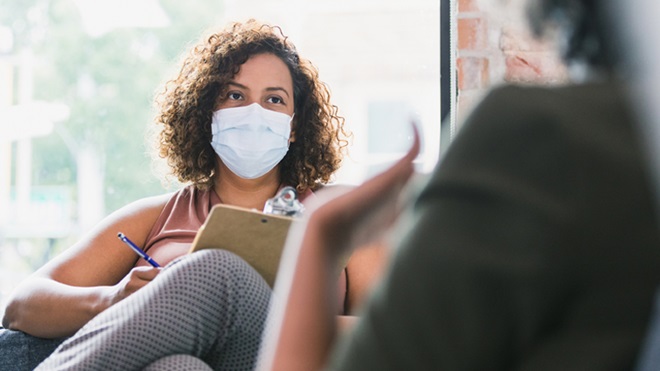 Terapeuta de máscara a ouvir um paciente e a tirar notas