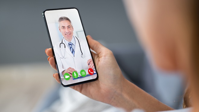 Mão feminina a segurar um telemóvel com a imagem de um médico