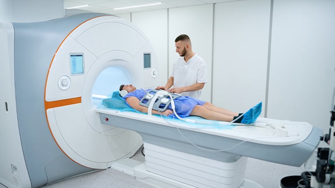 Paciente num aparelho de grandes dimensões, faz um procedimento médico num hospital, com um enfermeiro ao lado