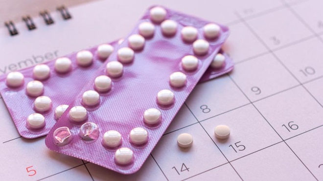 Grande plano de 2 lamelas de medicamentos de cor lilás, sobre um calendário - alusão à toma da pílula contracetiva