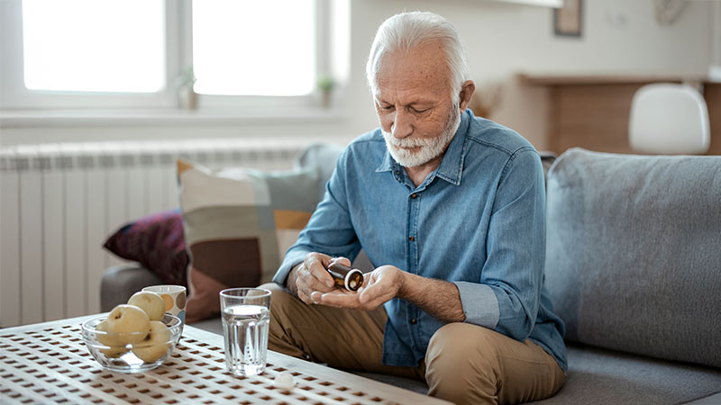 Homem sentado no sofá com um frasco de comprimidos