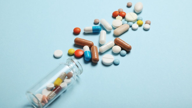 frasco transparente com medicamentos coloridos derramado sobre um fundo azul claro