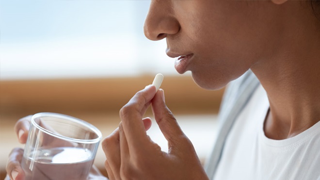 Grande plano de mulher a tomar um comprimido e a segurar um copo de água