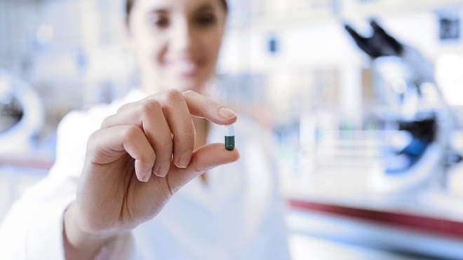 Mulher num ambiente de laboratório, com uma cápsula azul entre os dedos