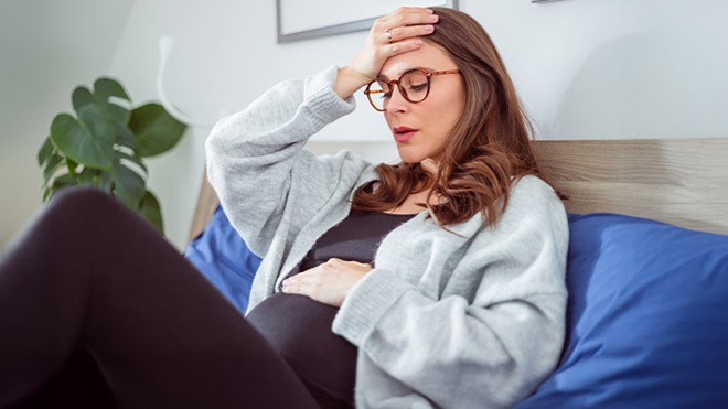 Grávida sentada no sofá com dores de cabeça