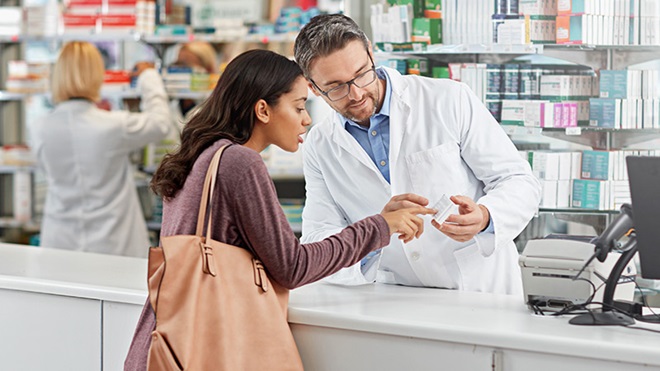 Rapariga na farmácia a ver caixa de medicamento com o farmacêutico