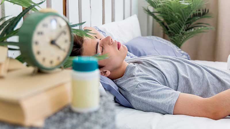 Homem a dormir com despertador e frasco de comprimidos