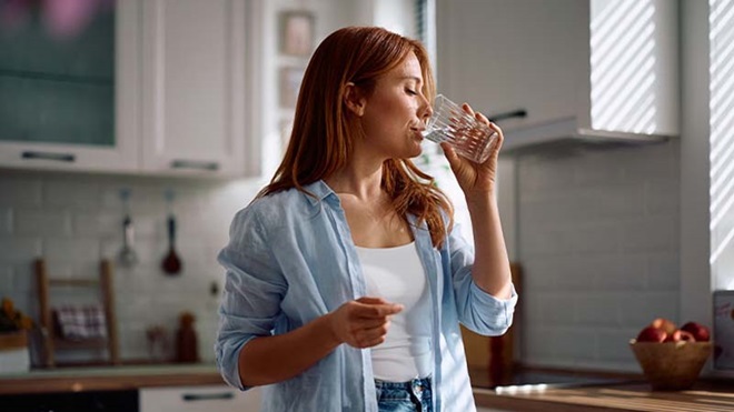 Plano médio de mulher, na sua cozinha a beber água