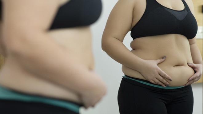 Mulher com excesso de peso vê-se ao espelho e aperta a zona da barriga