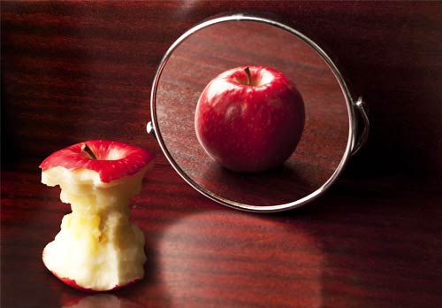 Uma maçã quase toda comida em frente a um espelho, mas o reflexo é o de uma maçã inteira, numa alusão à visão distorcida que as pessoas com anorexia têm do seu corpo.