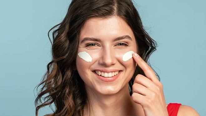 Grande plano de rosto de mulher a aplicar creme na cara - alusão a protetores solares de rosto