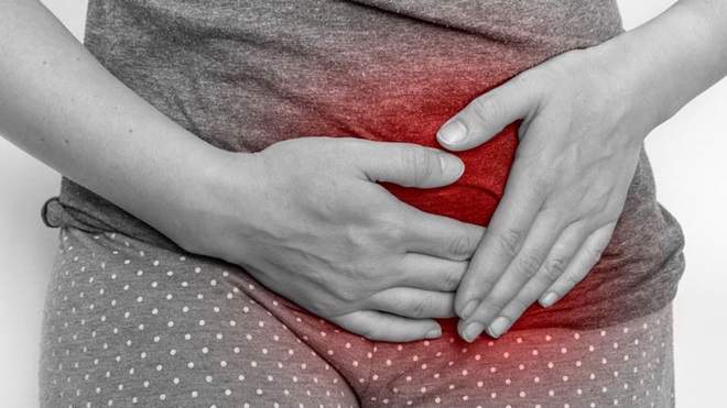 Imagem a preto e branco do abdómen de uma mulher que tem as mãos sobre a zona do ventre que está a vermelho, porque sofre de dismenorreia.