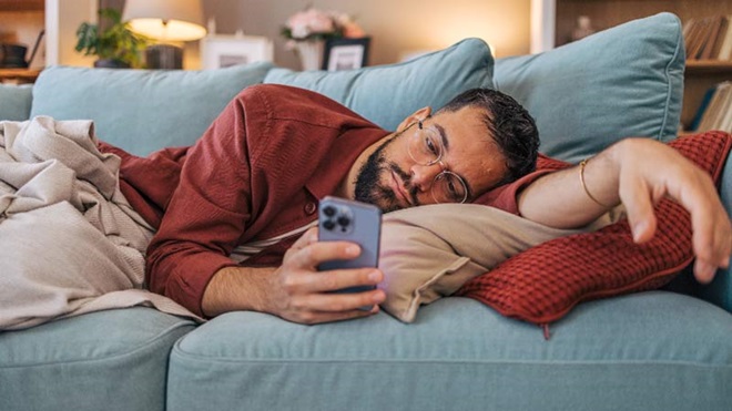 Adulto com ar deprimido, deitado num sofá, com um telemóvel na mão