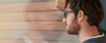 Homem encostado contra um vidro, vendo-se o seu reflexo, com ar deprimido