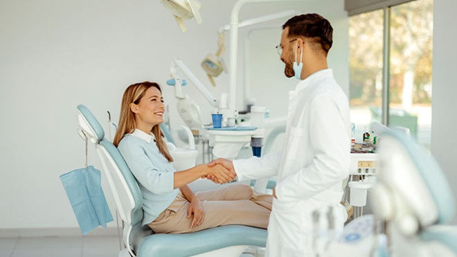 Consultório de dentista, com mulher sentada na cadeira a apertar a mão ao dentista