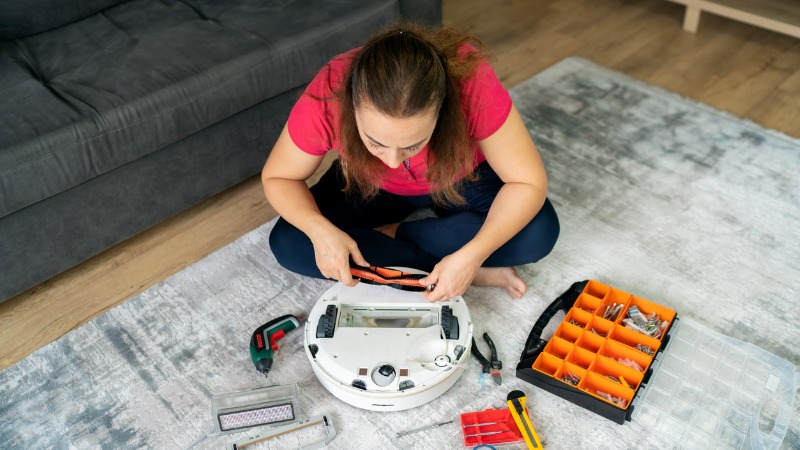 Mulher sentada no chão da sala tenta reparar aspirador.
