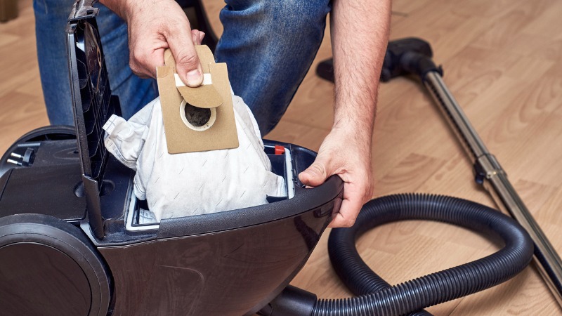 Homem troca o saco do aspirador.