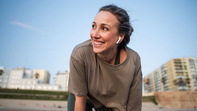 Mulher jovem a correr no exterior faz uma pausa; tem auriculares brancos nos ouvidos