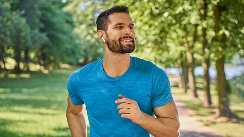 Homem jovem a correr num parque com auriculares de desporto