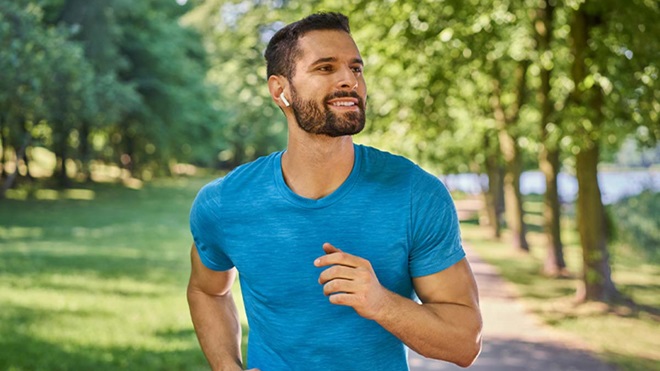 Homem jovem a correr num parque com auriculares de desporto