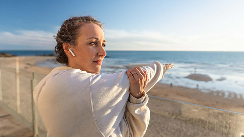 Mulher a fazer alongamentos na praia com auriculares sem fios nos ouvidos