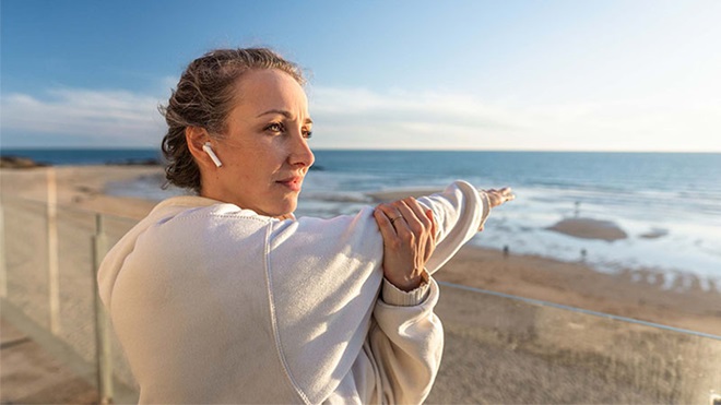 Mulher a fazer alongamentos na praia com auriculares sem fios nos ouvidos