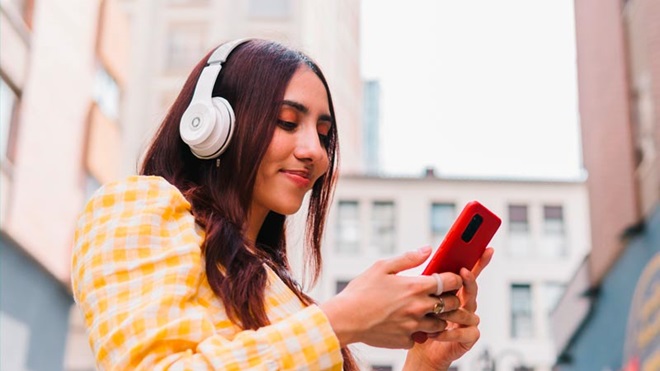 Mulher com headphones na cabeça ouve algo do telefone móvel que segura na mão - alusão a serviços de streaming audio