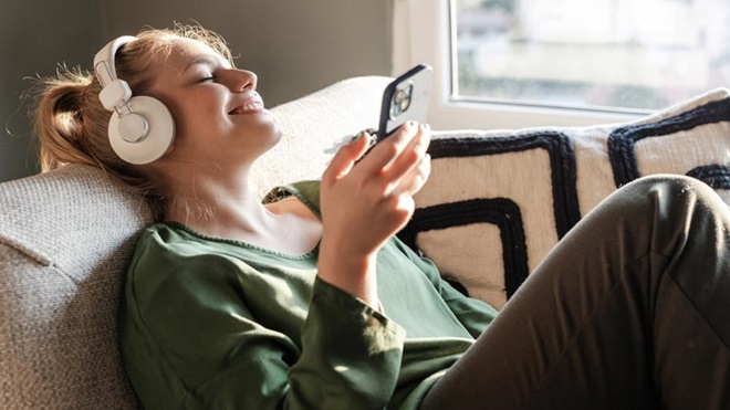 Jovem mulher a ouvir música no smartphone, com auscultadores de almofadas, recostada no sofã